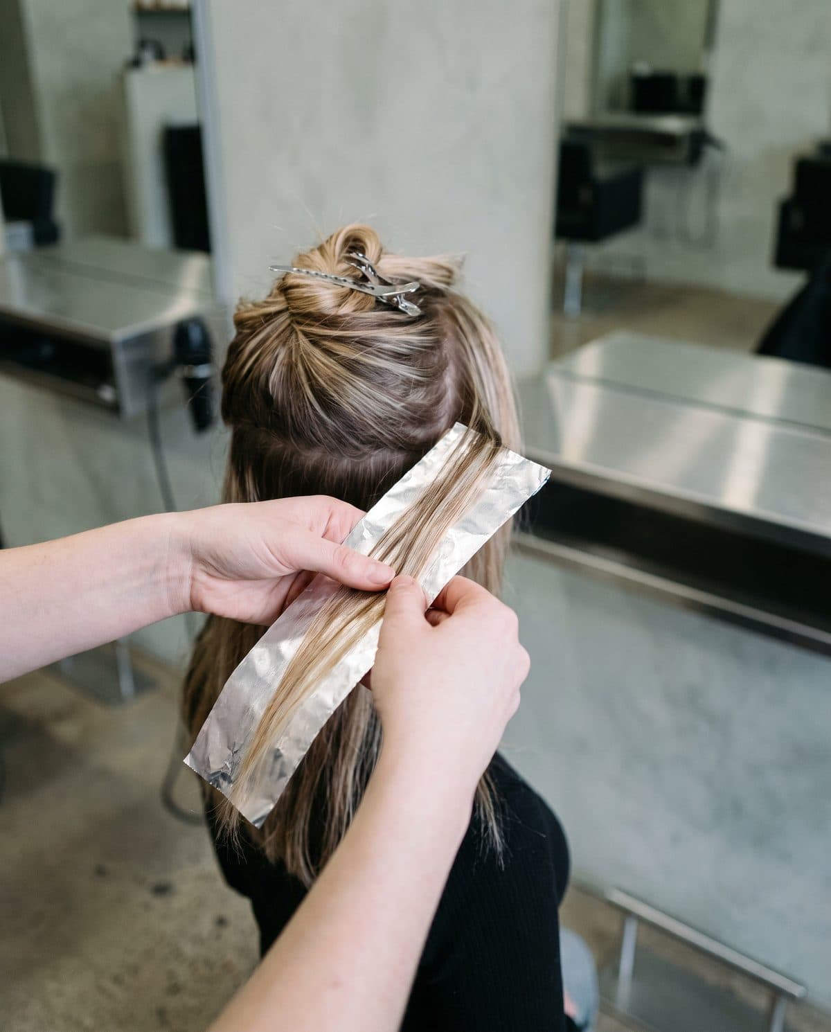A stylist's hands weaving a fine section of hair into a foil