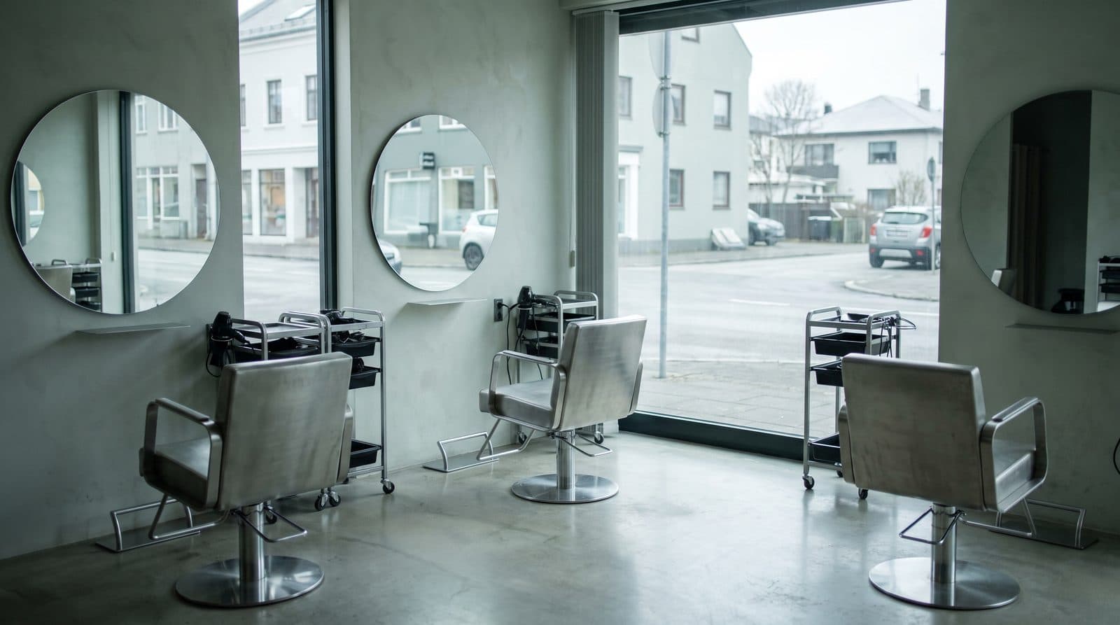 The salon from the back of the room: three empty chairs at their mirrors, the street beyond the window