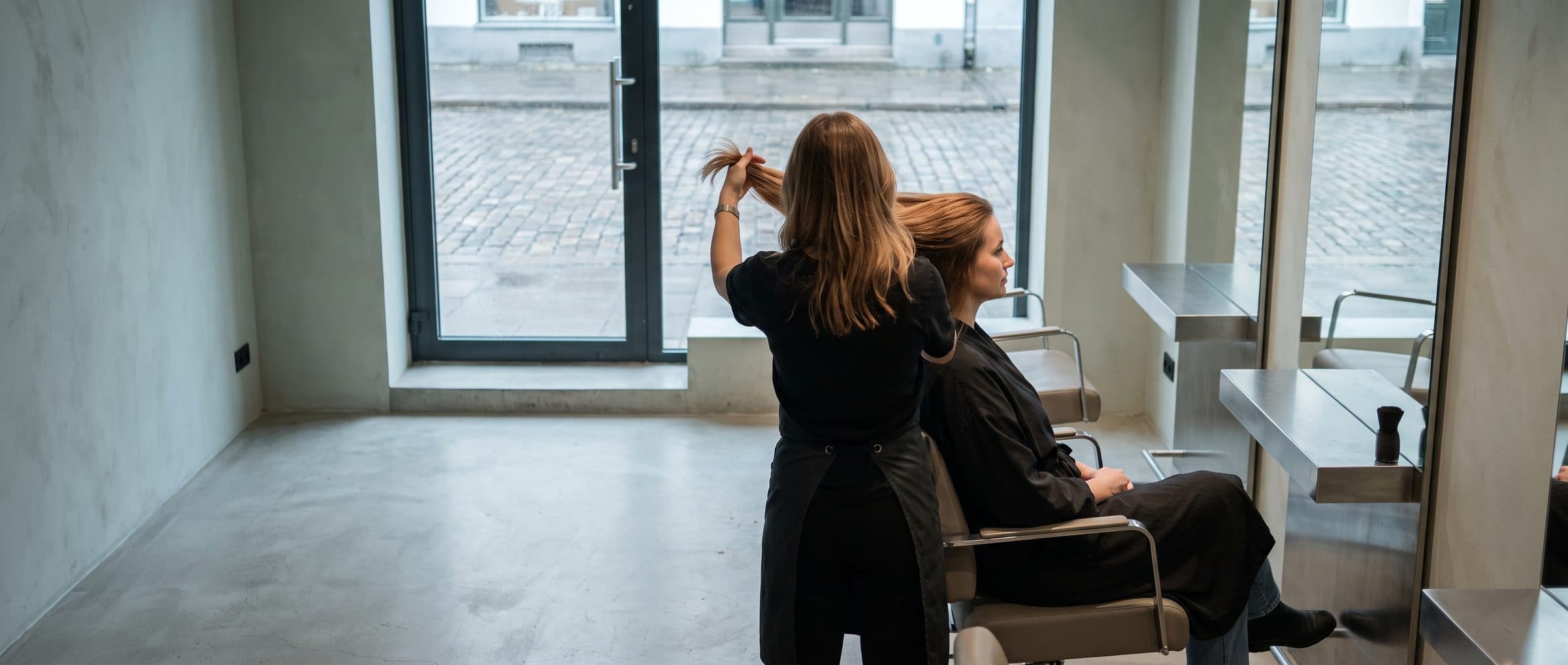 A stylist holding a section of freshly coloured hair up to the front window in daylight