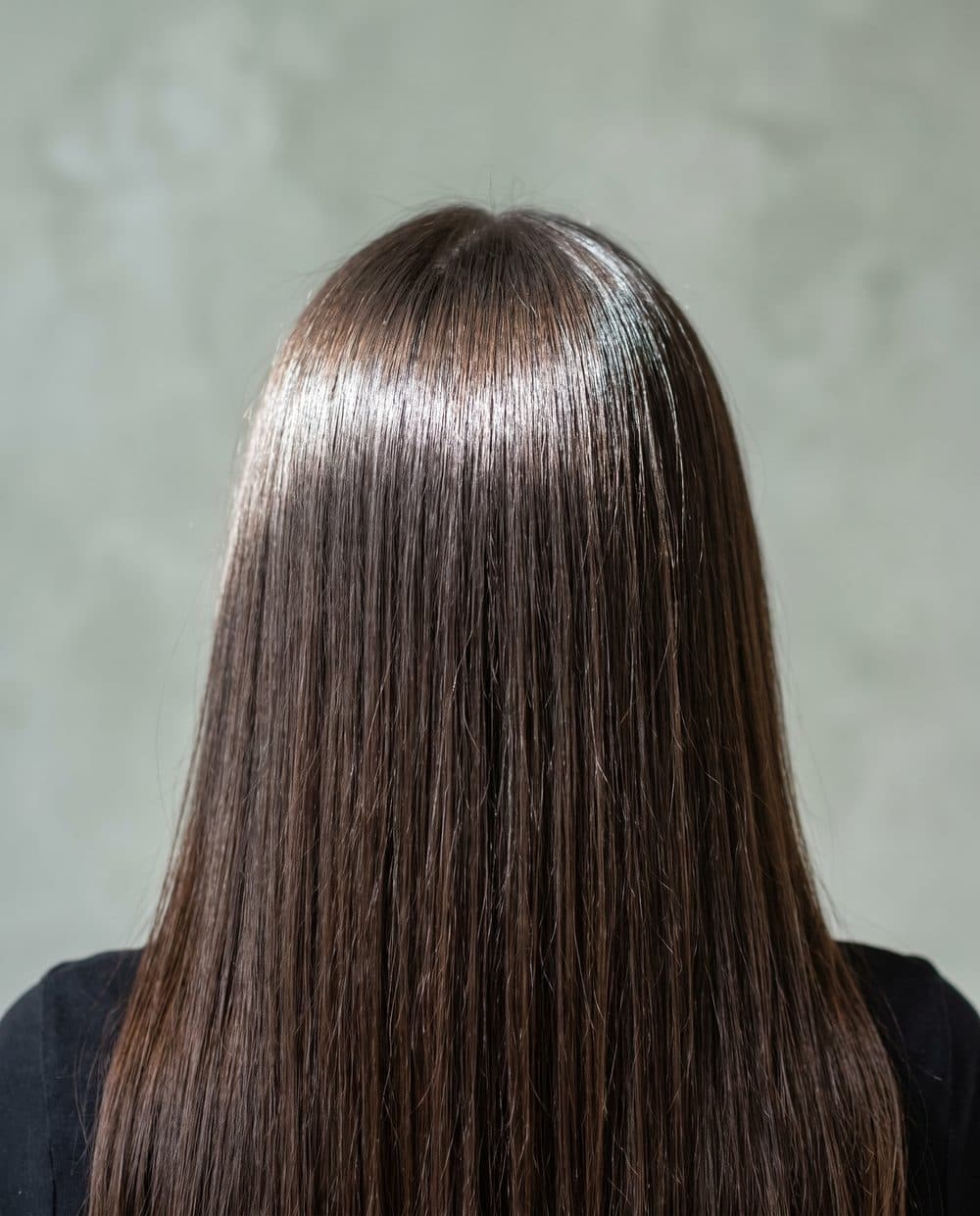 Dark brown hair after a clear gloss, a bright unbroken band of daylight running across the crown
